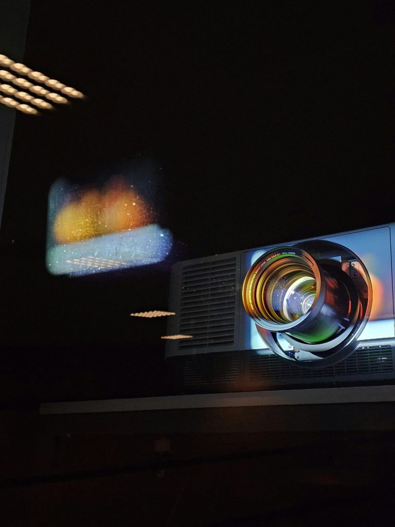 Projector lens reflecting colorful light pattern onto a dark wall.