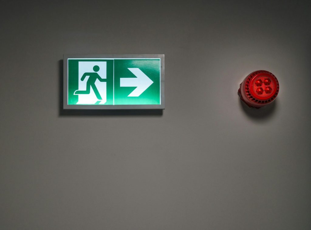 A brightly lit exit sign and alarm in an indoor corridor, indicating emergency escape route.